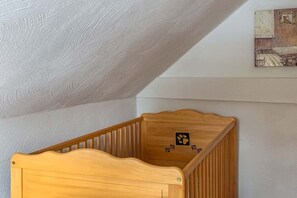 Ein hölzernes Kinderbett in einem Raum mit schrägem Dach und einem gerahmten Bild an der Wand.