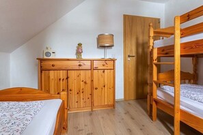Huoneessa on kerrossänky, puinen vaatekaappi, lamppu ja pieni koriste-esine lipaston päällä.