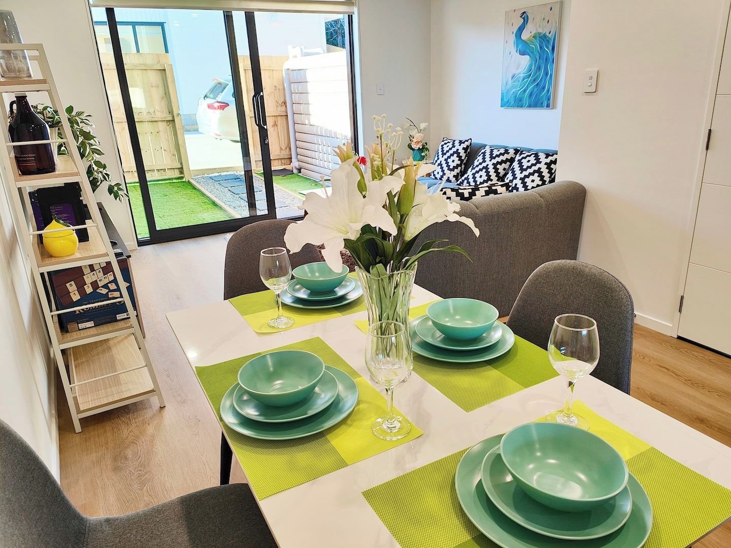 A dining area with a table set for two, green plates, and a vase with flowers.