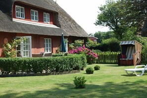 A thatched-roof house with a well-maintained garden, a small shed, and a white lounge chair. - Holiday apartment with 1 bedroom (Borgsum)