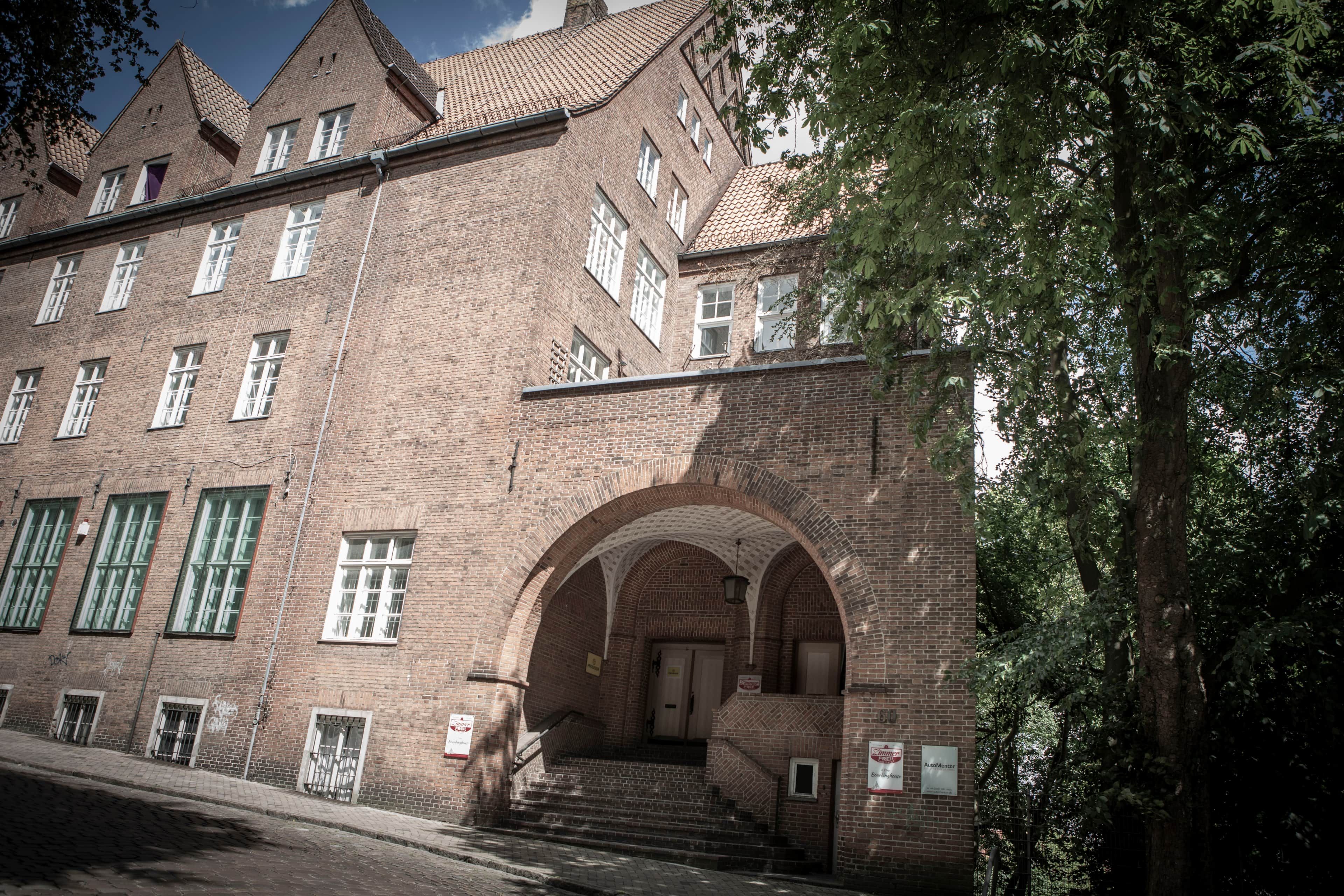 Ein großes Backsteingebäude mit zahlreichen Fenstern und einem zentralen Rundbogenportal.