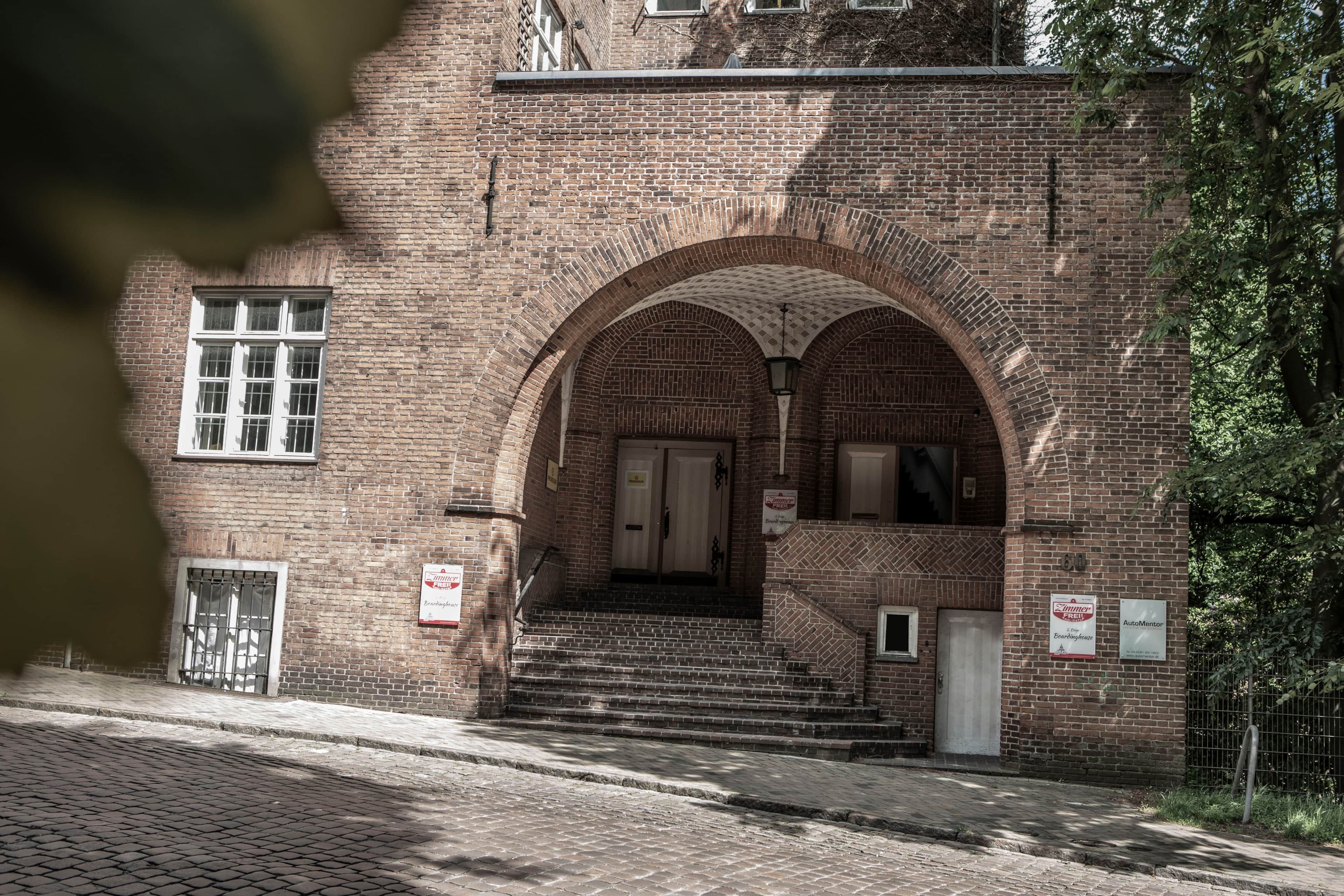 Ein Backsteinhaus mit einem zentralen Rundbogen und einer Treppe zum Eingang, mit einem Schild, das ein Pension angibt.