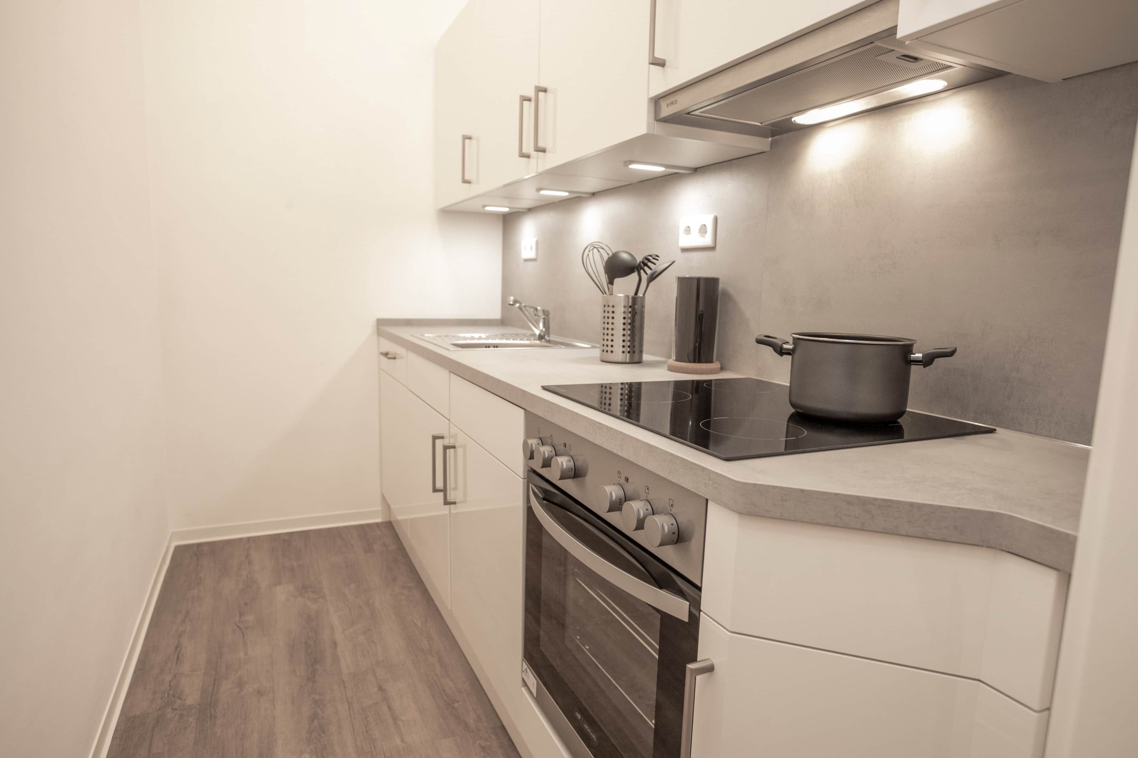 A modern kitchen with white cabinets, a stainless steel range hood, a built-in oven, and a black induction cooktop.
