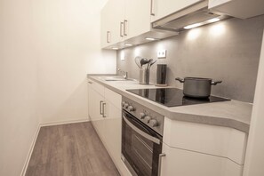 Une cuisine moderne avec des armoires blanches, une hotte en acier inoxydable, un four encastré et une plaque de cuisson à induction noire.