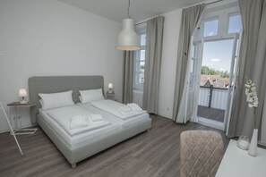 Un dormitorio moderno con cama, lámparas de noche, vistas al exterior y un balcón.