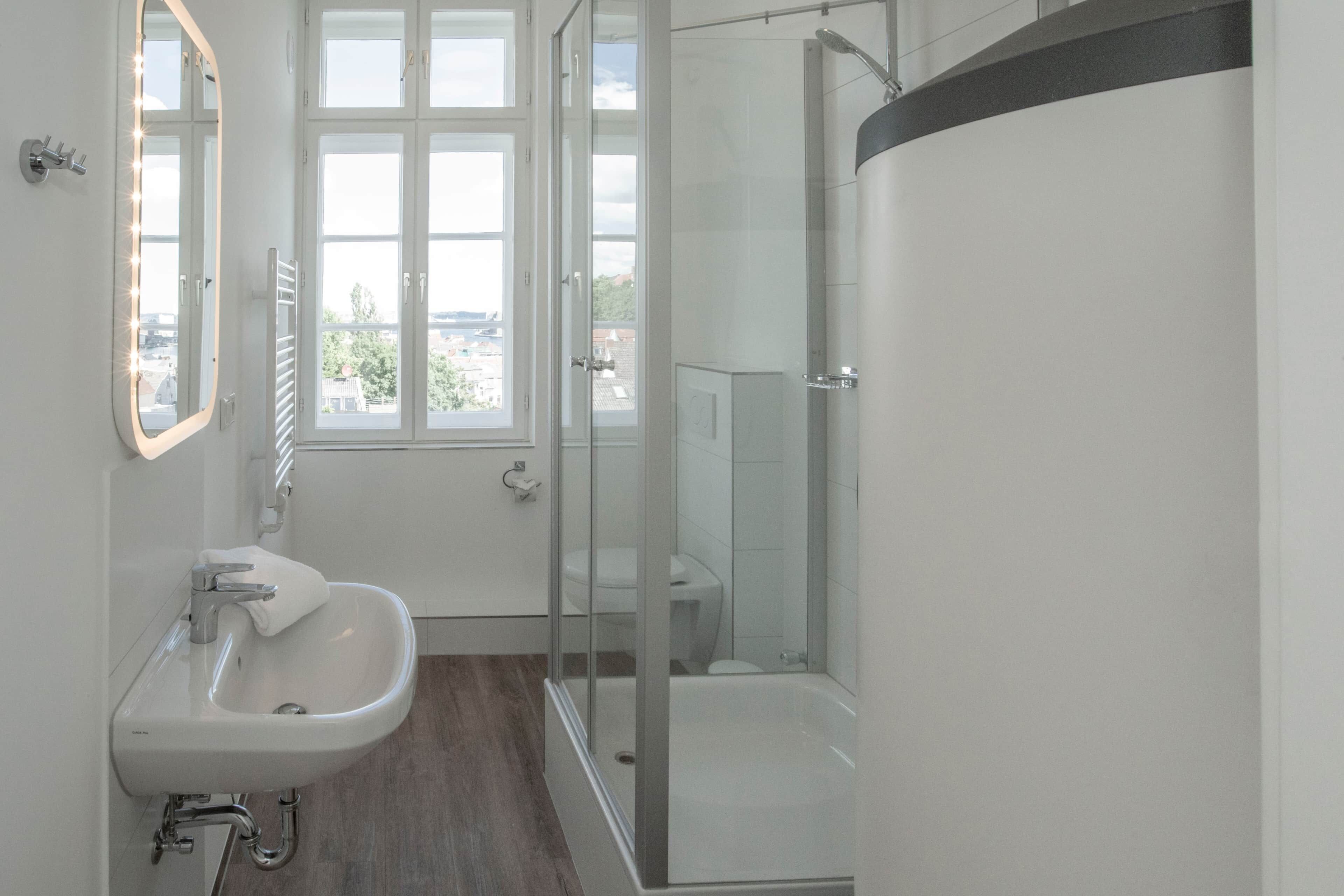 Ein modernes Badezimmer mit einem weißen Waschbecken, einem Spiegel und einer Duschkabine aus Glas.