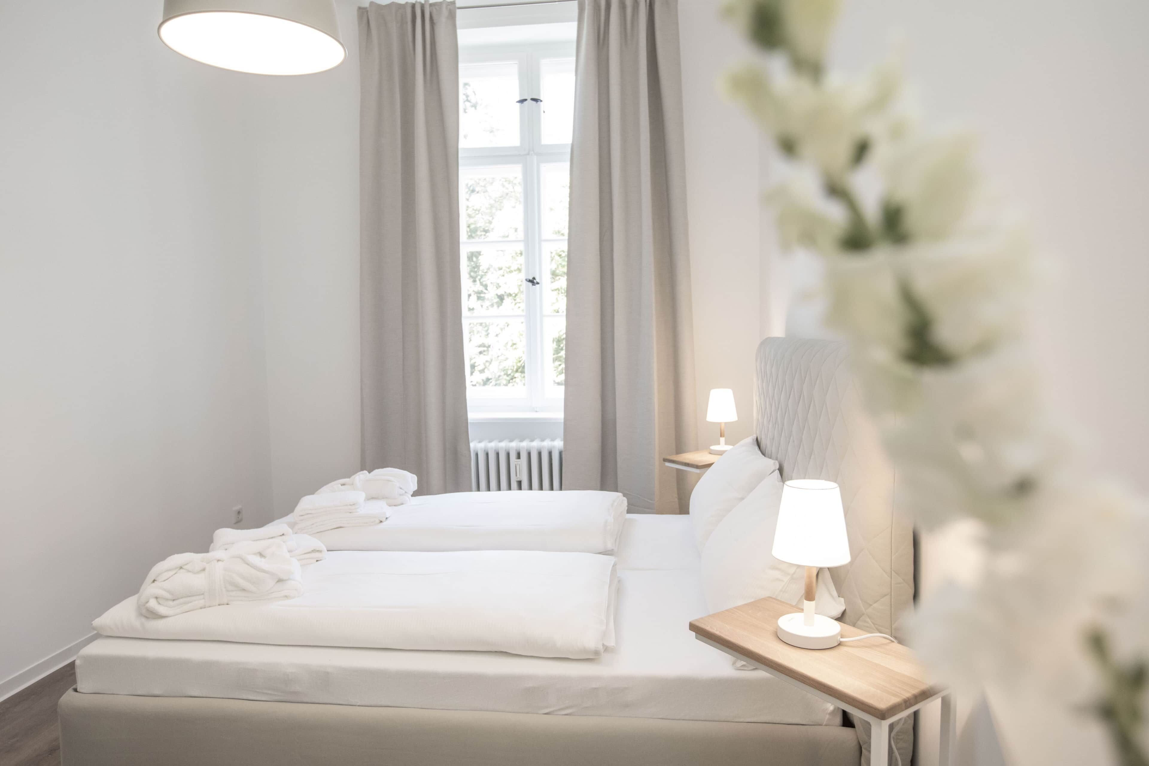 Une chambre d’hôtel avec un lit, une table de chevet avec une lampe et une fenêtre avec des rideaux.