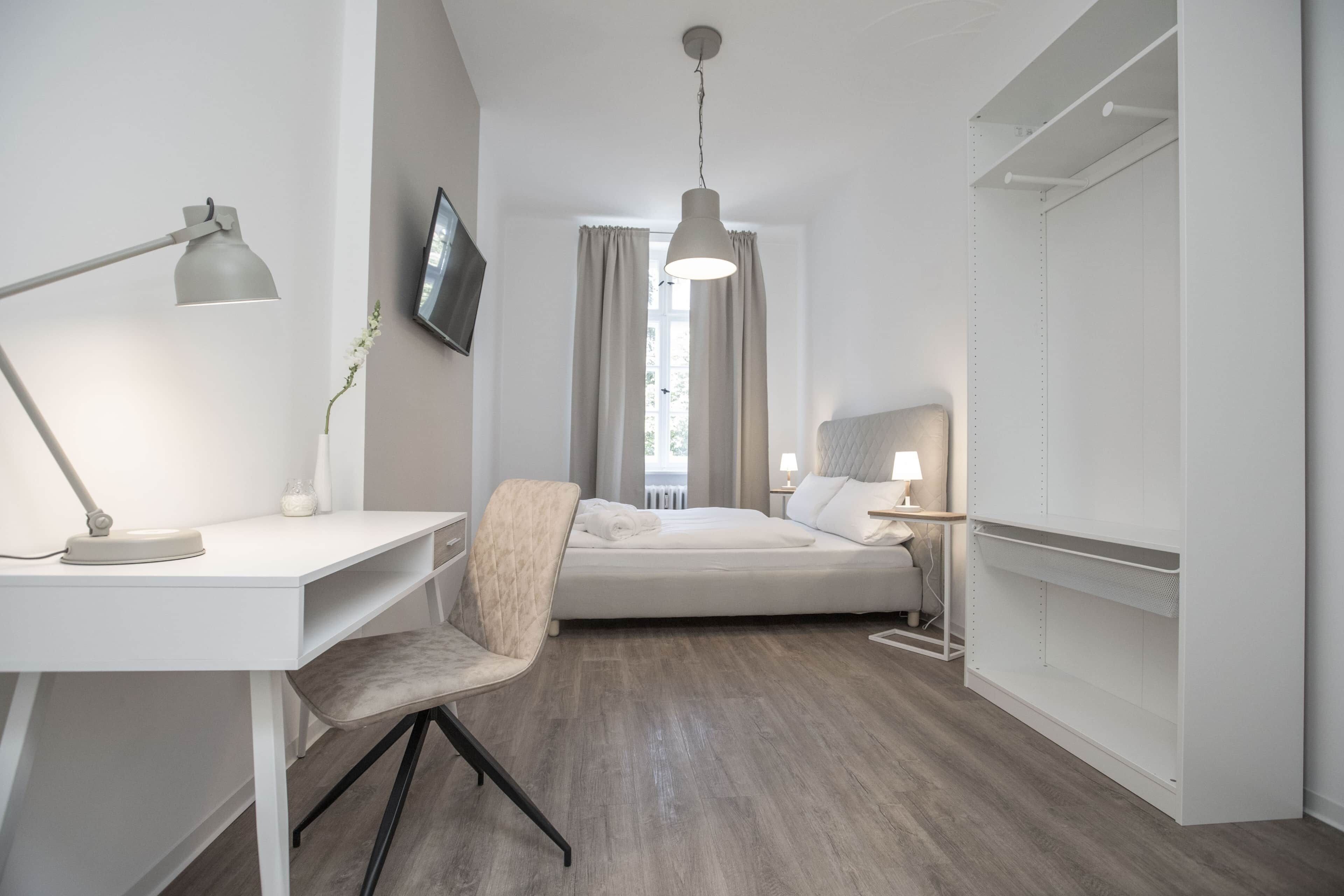 Ein modernes Hotelzimmer mit Bett, Schreibtisch, Stuhl und einem an der Wand befestigten Fernseher.