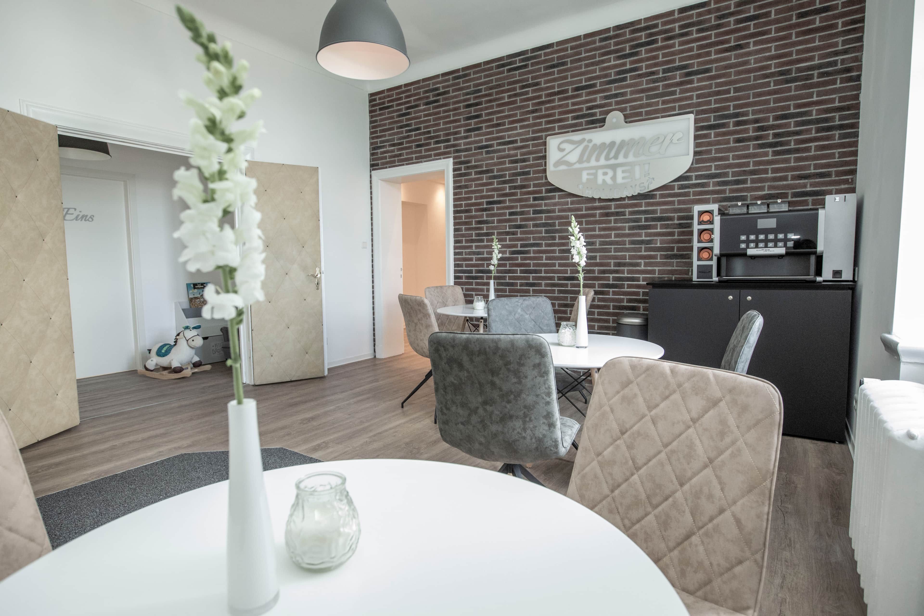 A modern dining area with a brick wall, a white table, and grey upholstered chairs.
