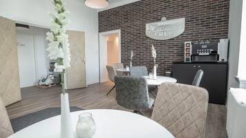 A modern dining area with a brick wall, a white table, and grey upholstered chairs.