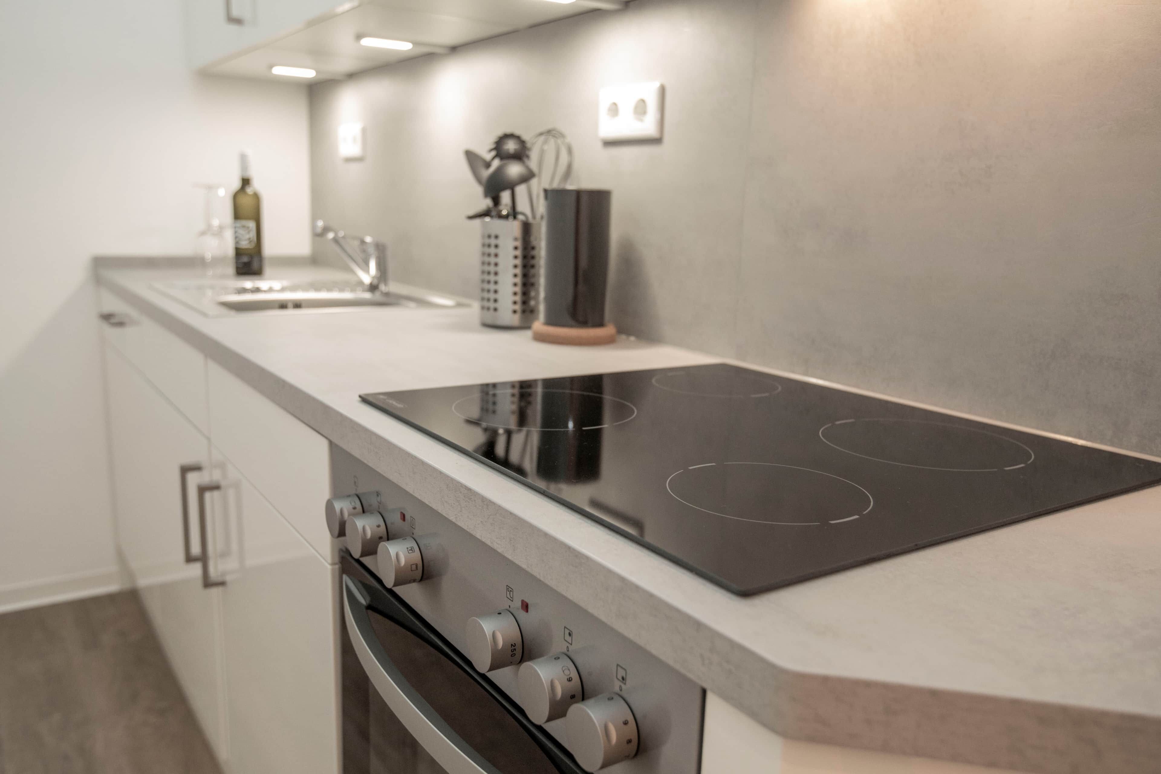 Una cocina moderna con estufa, horno integrados y una botella de vino en la encimera.