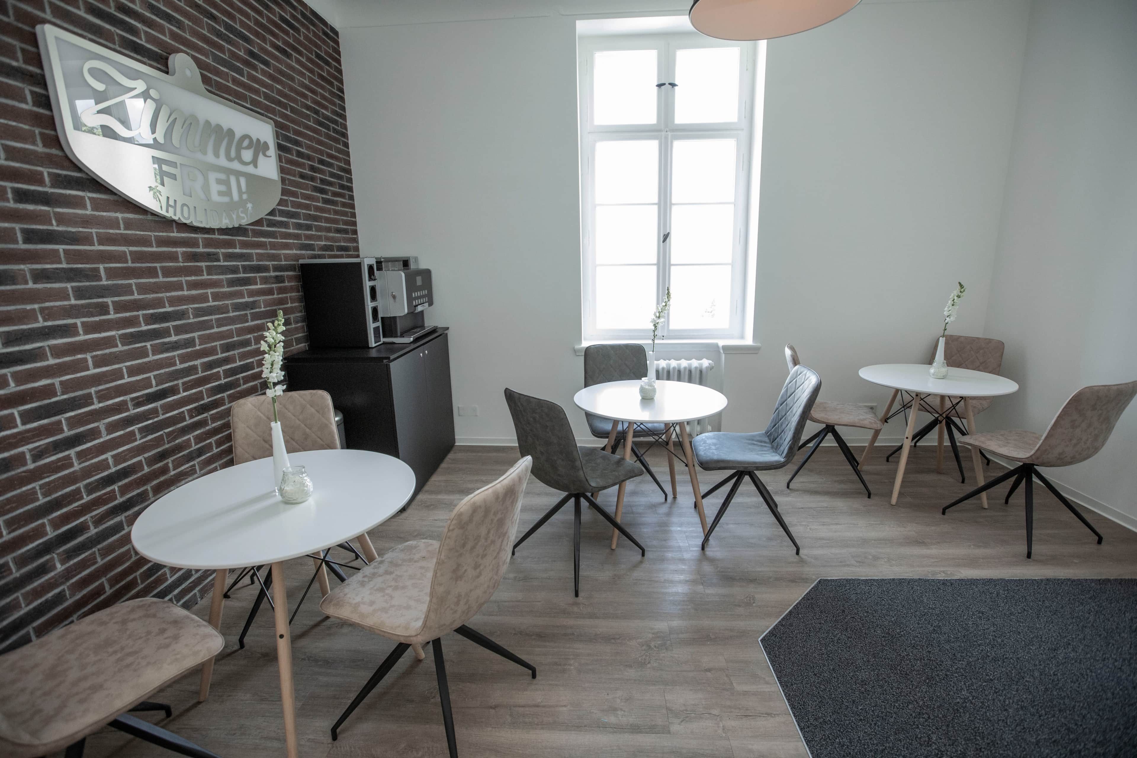 Ein modernes Interieur mit einer Ziegelwand, einer Kaffeemaschine und mehreren runden Tischen mit Stühlen.