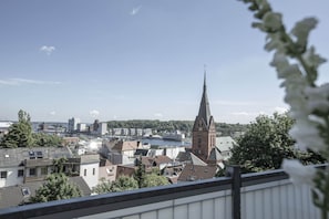 Un paysage urbain avec un clocher d’église imposant, des immeubles résidentiels et une étendue d’eau.