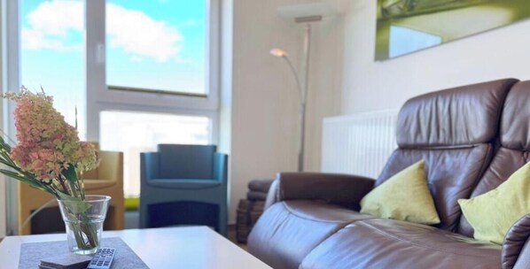 Ein Wohnzimmer mit einem braunen Ledersofa, einer Glasvase mit Blumen, einem Tisch und einem Sessel.