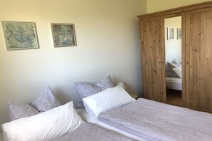 A bedroom with two beds, a wooden wardrobe, and two framed artworks on the wall. - Anchor in House Fördeglück (Glücksburg)