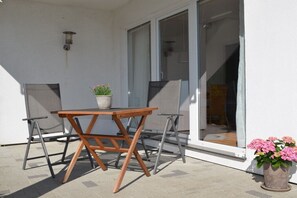 An outdoor patio with a wooden table and chairs, a potted plant, and a sliding glass door leading to an interior space. - Anchor in House Fördeglück (Glücksburg)