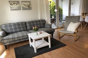 Ett vardagsrum med en soffa i rutigt tyg, ett vitt soffbord och en fåtölj i trä.