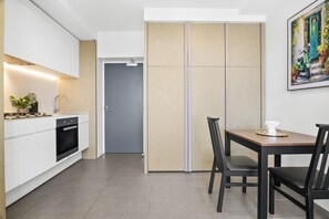 A modern kitchen with white cabinets, a built-in oven, and a dining area with a wooden table and chairs. - High-Rise 1-Bed Apartment in Docklands (Docklands)