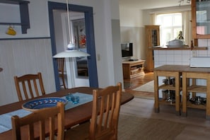 Un comedor con una mesa y sillas de madera, un televisor y una cocina con alacenas y estufa.