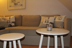 A room with a sofa, two white tables, and pillows with 'COAST 53' text. - Shell in House Fördeglück (Glücksburg)