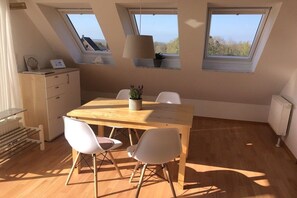 A room with a wooden dining table, two white chairs, a ceiling lamp, and skylights. - Shell in House Fördeglück (Glücksburg)