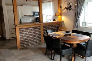A dining area with a brick partition, a wooden table, and black chairs. - Holiday home in Hooksiel with swimming pool (Hooksiel)