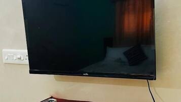 Un televisor de pantalla plana montado en una pared con un control remoto sobre un estante rojo.