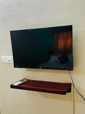Televisor de pantalla plana penjat a la paret amb un comandament a prestatge vermell a sota.