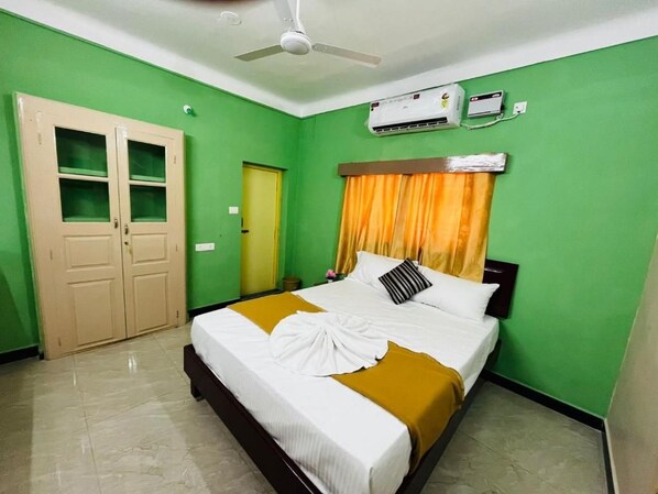 A hotel room with a bed, a wardrobe, an air conditioning unit, and a ceiling fan.