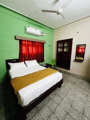 Een hotelkamer met een bed, een airconditioner, een plafondventilator, een deur en een klein tafeltje.