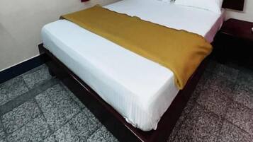 Una habitación de hotel con cama, cortina roja, unidad de aire acondicionado y estante pequeño en la pared.