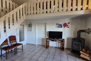 A living room with a wooden staircase, a television, a fireplace, and a red upholstered chair. - Holiday home in Zandt with swimming pool (Zandt)