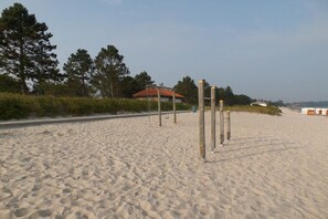 En sandstrand med en träkonstruktion och en byggnad med ett rött tak i bakgrunden.