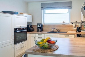 A modern kitchen with white cabinets, a built-in oven, a coffee maker, and a fruit bowl on the counter. - Holiday home Sailing view Luv (Glücksburg)