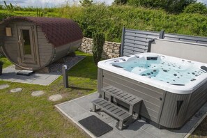 A hot tub with steps leading up to it, a covered outdoor shower, and a stone wall in the background. - Holiday home Sailing view Luv (Glücksburg)