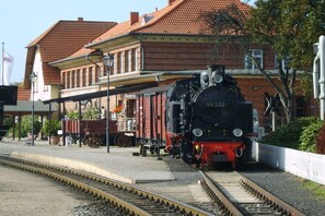 A vintage steam locomotive at a railway station with a brick building in the background. - Holiday apartment Villa Strandkuss 322247 (Kühlungsborn)