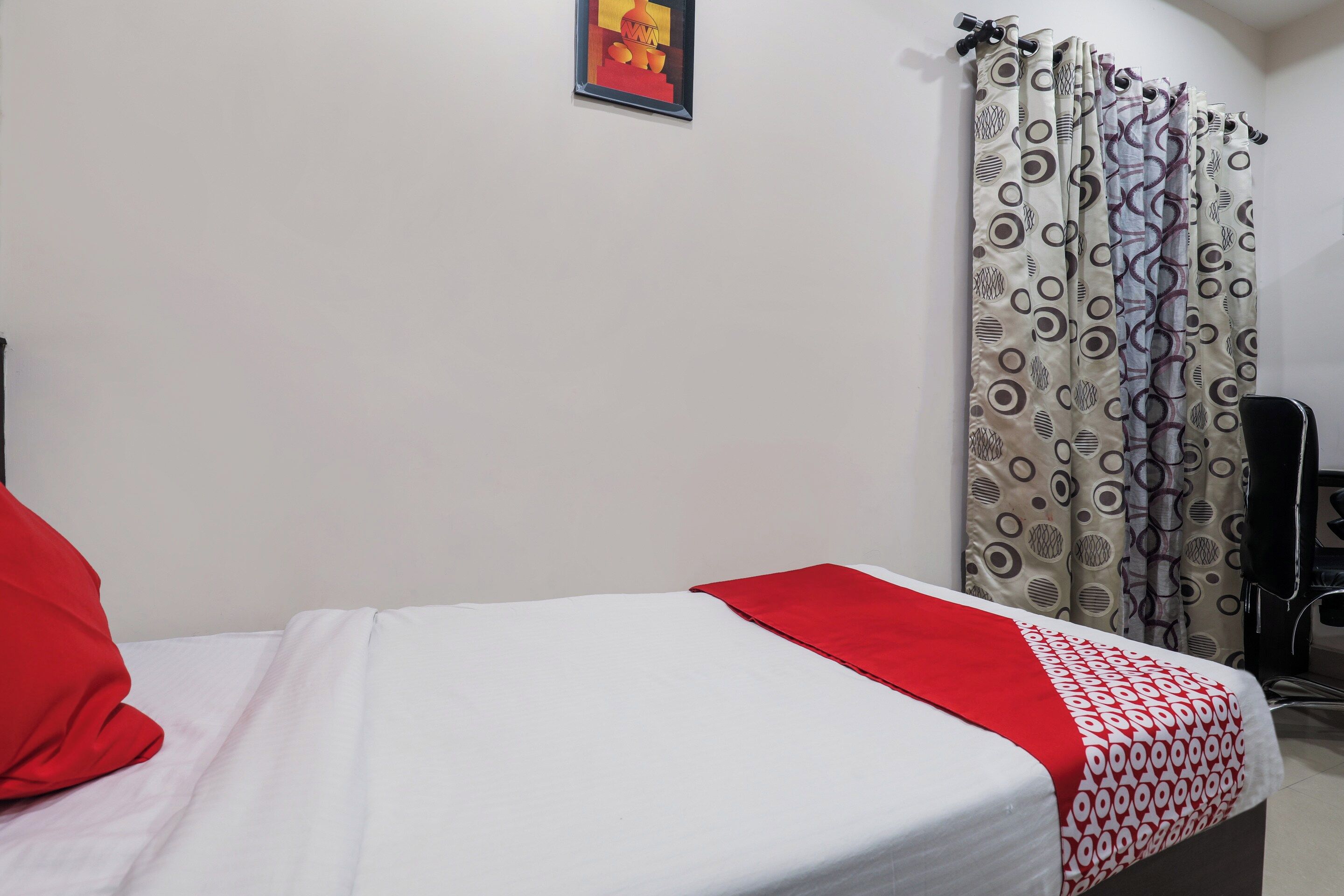 Uma cama de solteiro com edredom branco e vermelho, um travesseiro vermelho e cortina estampada.