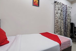 Uma cama de solteiro com edredom branco e vermelho, um travesseiro vermelho e cortina estampada.