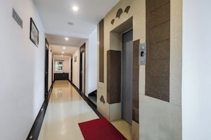 Corredor de hotel com carpete vermelho, elevador fixado na parede e placa indicando o segundo andar.