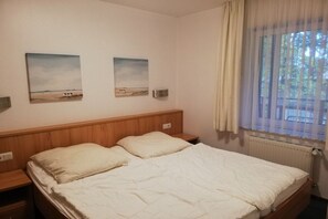 A bedroom with a wooden headboard, two bedside tables, a bed with white bedding, and two landscape paintings on the wall. - Holiday apartment with 1 bedroom (Koserow)