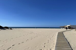A sandy beach with footprints, a wooden boardwalk, and a clear blue sky. - Apartment with 1 bedroom (Chia SU, Domus de Maria)