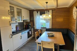 A compact kitchen with a dining area, wooden walls, and a clock on the wall. - Holiday apartment by the lake with lake view, upper floor (Arrach)