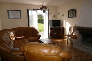 Een woonkamer met een leren bank, een televisie, een open haard en uitzicht op het groen.