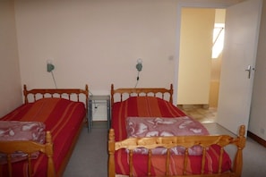 Een kamer met twee enkele bedden, een kleine tafel en een deur naar een andere kamer.