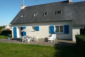 A house with a sloped roof, a patio with outdoor furniture, and a small garden area. - Lambezen-maison aux volets bleus (Camaret sur mer)