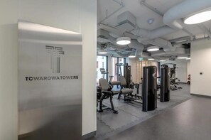 Una sala de gimnàstica amb equip d'exercici, una paret amb la inscripció 'TOWAROWATOWERS' i un sostre amb conductes a la vista.