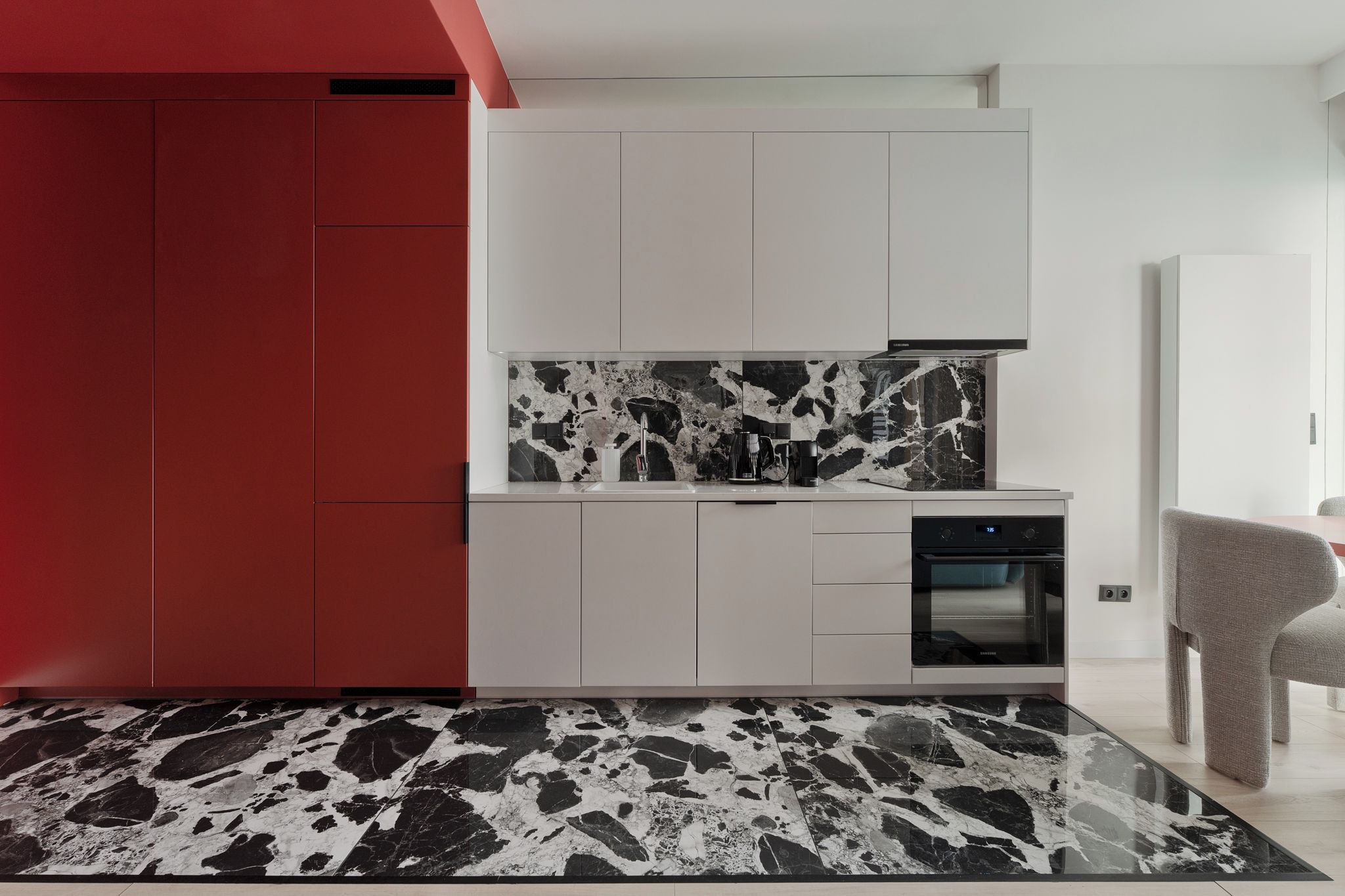 A modern kitchen with a red accent wall, white cabinets, a black and white marble backsplash, and a black oven.