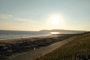Een kustlandschap met een strand, rotsachtige kustlijn en een heuvel in de verte.