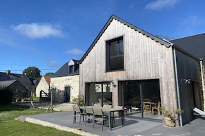 A modern building with a large glass door entrance, a patio with outdoor seating, and a stone facade. - Holiday home with 1 bedroom (Les Moitiers-d'Allonne)