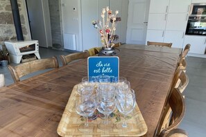 A round wooden dining table with a sign reading 'La vie est belle dans le cotentin' and six empty wine glasses on a tray. - Holiday home with 1 bedroom (Les Moitiers-d'Allonne)